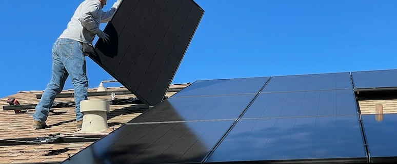 En man står på ett villatak och monterar solceller.